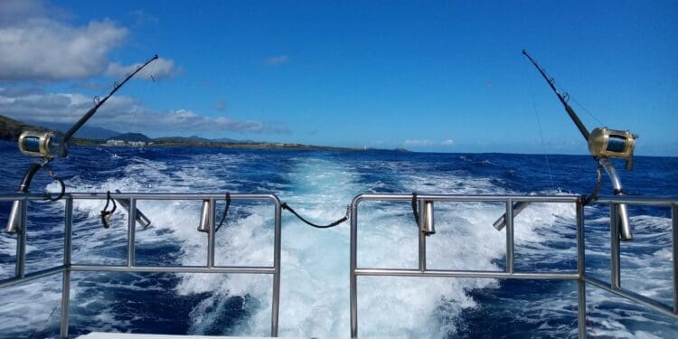 Fishing boat waves on ocean, distant shoreline view.