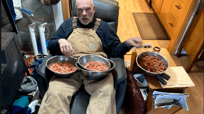 Man relaxing with bowls of shrimp indoors.