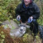 Mark posing with deer in forest.