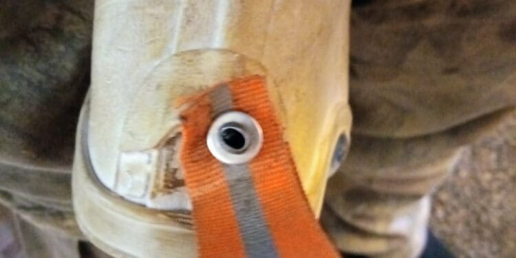 Worn rubber boot with orange strap and metal grommet repair