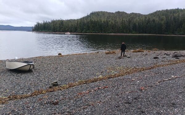 Person standing on rocky beach with small boat by calm bay