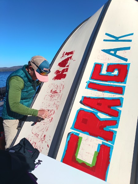 Person painting CRAIGAK letters on a boat hull