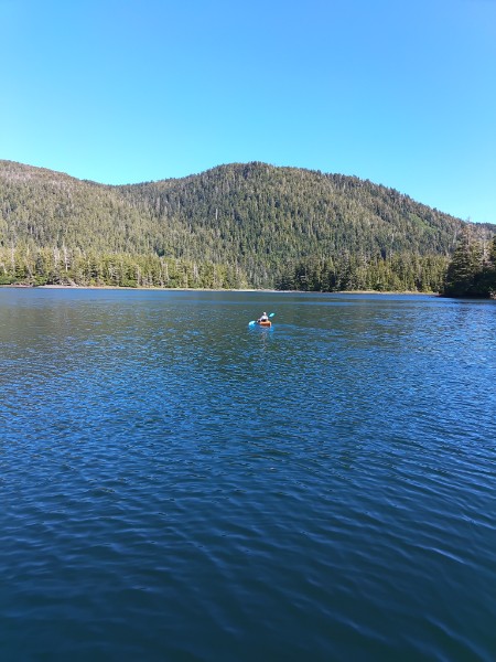 Kayaker paddling on calm mountain lake surrounded by forests