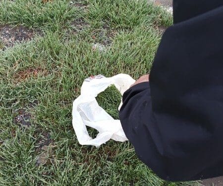 Person picking up plastic bag from frosty grass