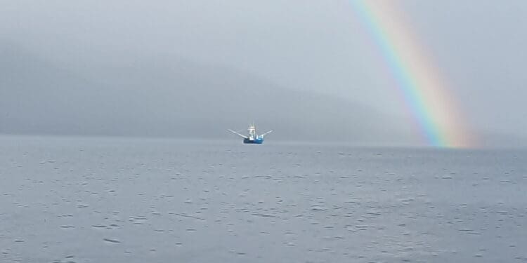 Fishing boat on calm ocean beneath a vibrant rainbow