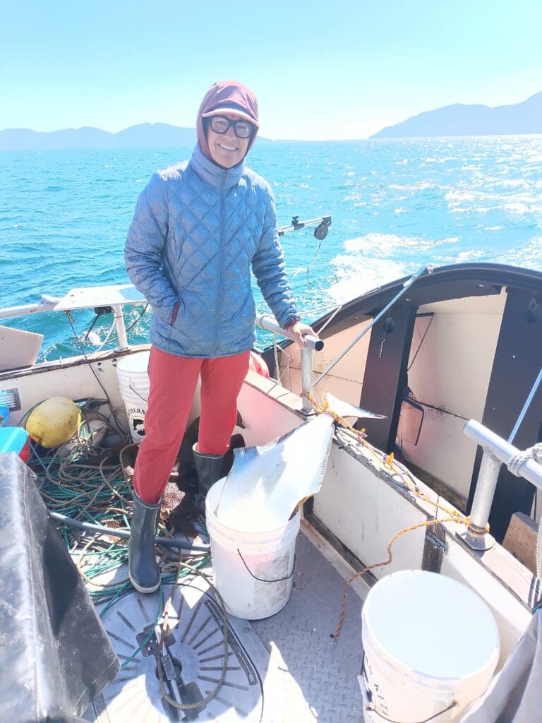 Smiling fisher on boat deck with large halibut catch