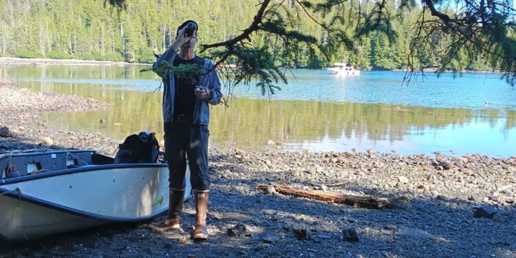Person standing on rocky shore beside canoe near forested lake